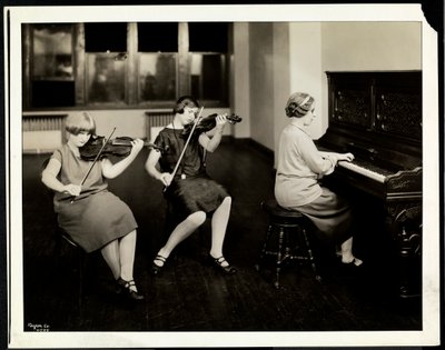 Gruppe von drei jungen blinden Frauen, eine am Klavier, zwei spielen Geige, bei der New York Association for the Blind, 111 East 59th Street, New York, 1926 von Byron Company